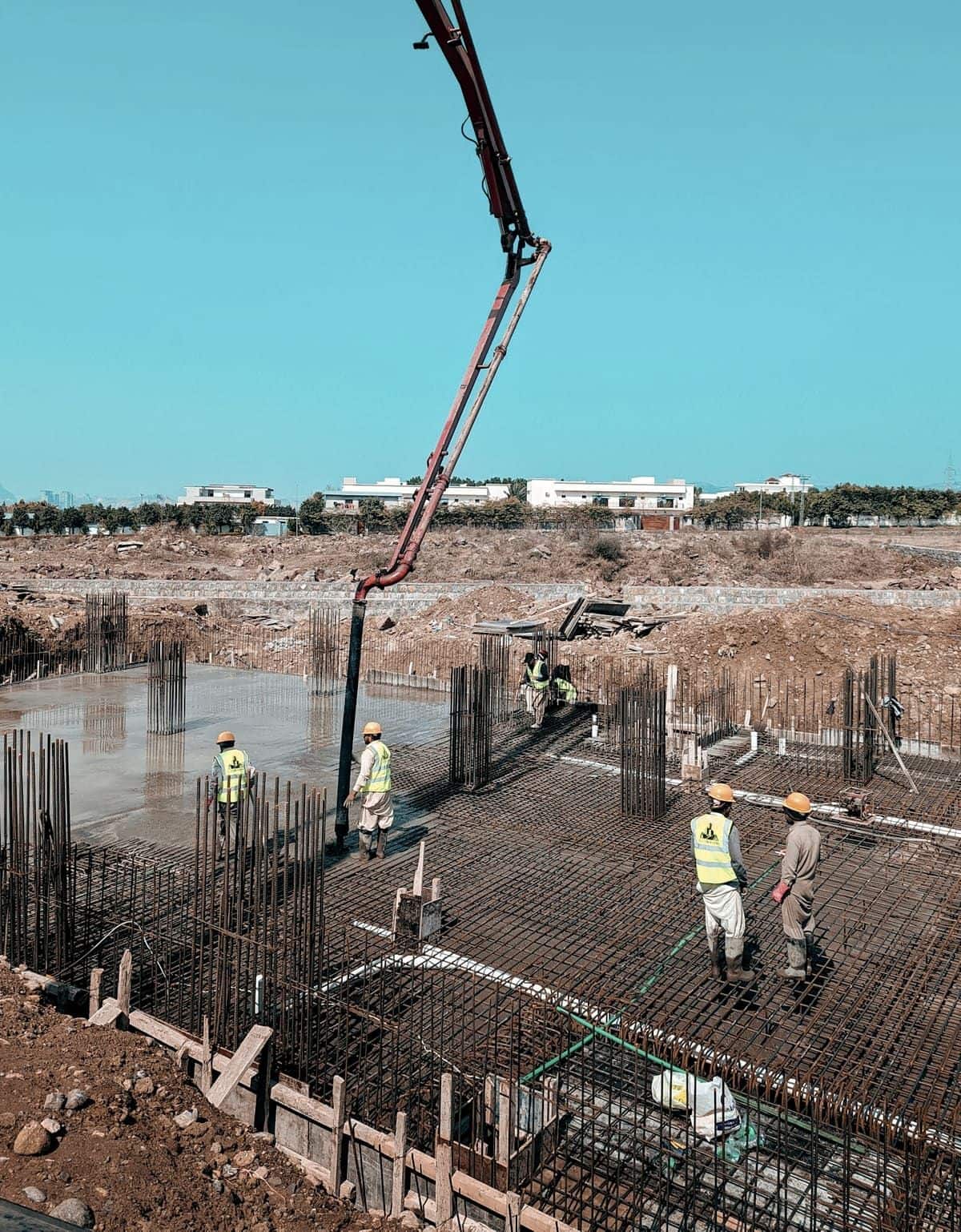 A concrete boom pump placing ready-mixed concrete into a reinforced raft foundation while site crew work the pour.